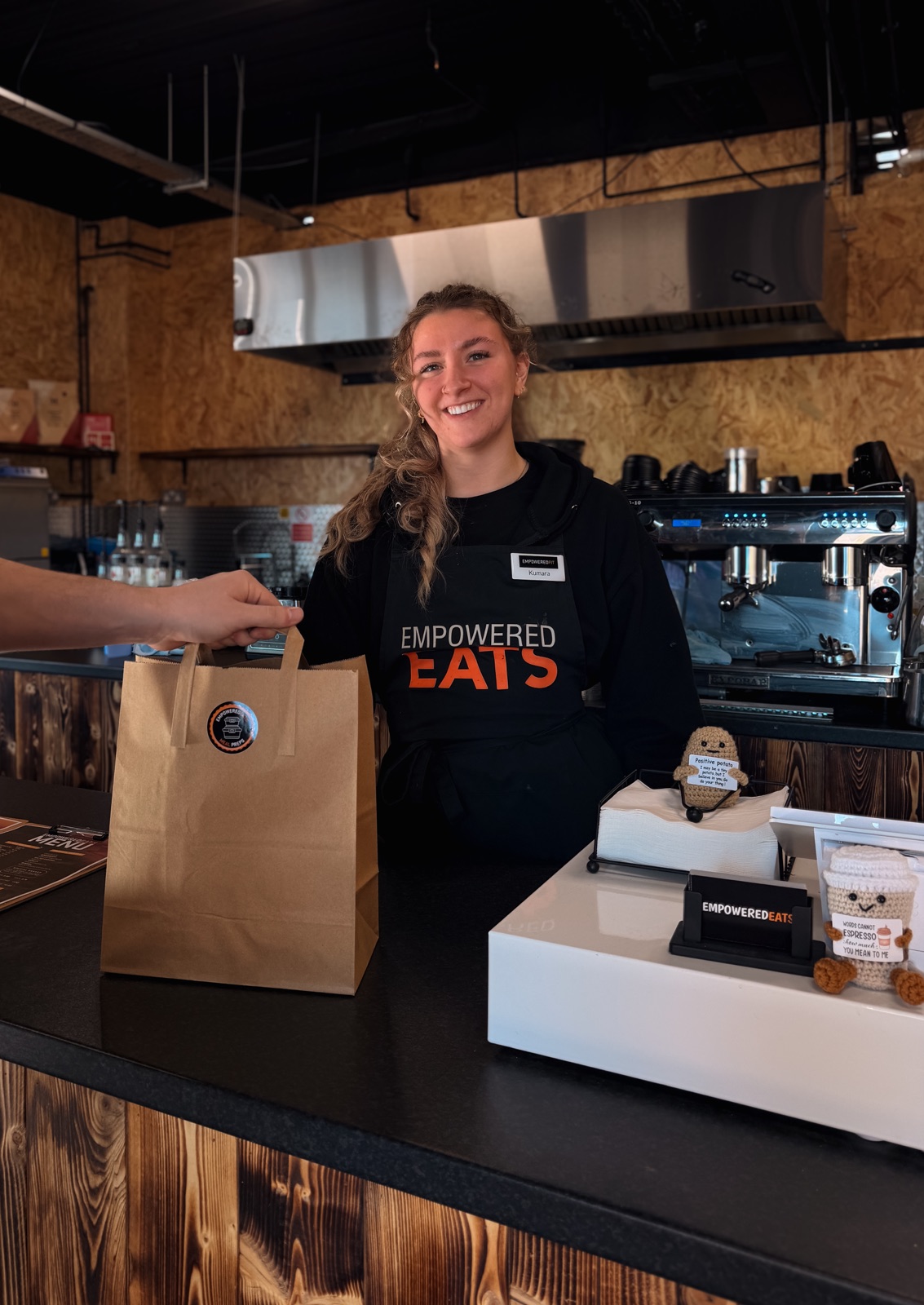 Empowered Eats cafe team handing a prepared meal bag to a customer in Liverpool